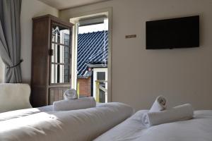 2 weiße Betten in einem Zimmer mit einem TV und einem Fenster in der Unterkunft Hofje van Maas in Zandvoort