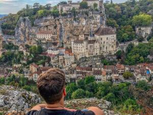 a man sitting on a mountain looking at a city at Hotel des Voyageurs in Rocamadour +14 photos