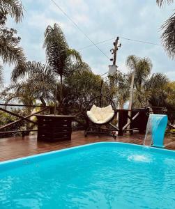 a blue swimming pool with a chair and palm trees at Pousada Altos do Rei in Praia do Rosa