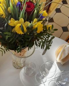 a vase of flowers on a table with wine glasses at Hôtel MADO in Le Crotoy