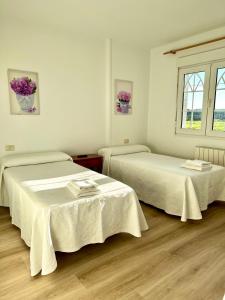 オ・ペドロウソにあるPensión Maruja *の白い壁とウッドフロアの客室で、ベッド2台が備わります。