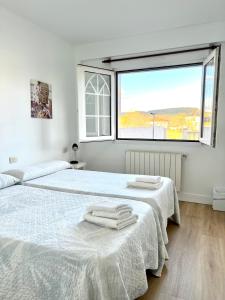 a white bedroom with two beds and a large window at Pensión Maruja * in O Pedrouzo