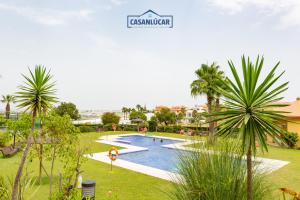 a swimming pool in a park with palm trees at Flamingo Golf A in Sanlúcar de Barrameda