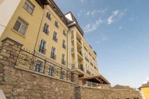 a large yellow building with a balcony on a stone wall at VIZUALIZA Residence Hotel in Plovdiv