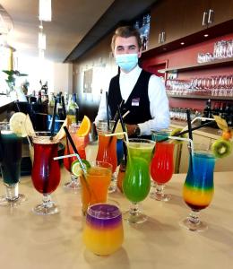 Um homem com uma máscara atrás de um bar com cocktails coloridos. em Bergwirtschaft Wilder Mann Hotel und Restaurant em Dresden