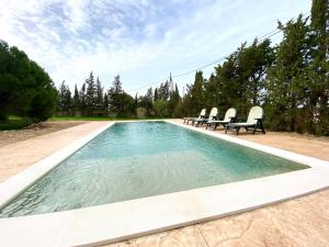 een zwembad met drie stoelen en een zonneklep bij Agradable casa de campo con piscina en la Barrosa in Chiclana de la Frontera