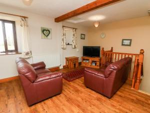 een woonkamer met 2 leren stoelen en een televisie bij Old Byre Cottage in Ravenstonedale
