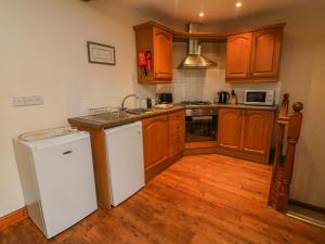 cocina con armarios de madera y nevera blanca en Hayloft Cottage en Kirkby Stephen