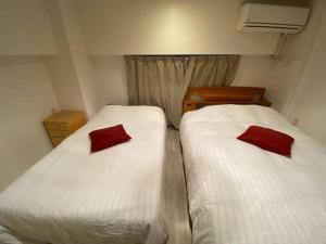 Habitación pequeña con 2 camas, sábanas blancas y almohadas rojas. en Takemura Building 107, en Tokio