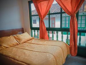 uma cama em frente a uma janela com cortinas vermelhas em H-OSTELLO LA MERIDIANA em Villa de Leyva