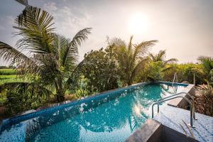 a swimming pool in a resort with palm trees at SaffronStays Happy Fields, Pune - luxury farmstay with farm to table food in Pune