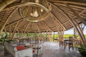 un grande ristorante con tetto di paglia, tavoli e sedie di Amarta Pesagi Retreat Tabanan a Tabanan