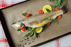 a fish sitting on a cutting board with vegetables at Casa Tödi Restaurant Hotel in Trun