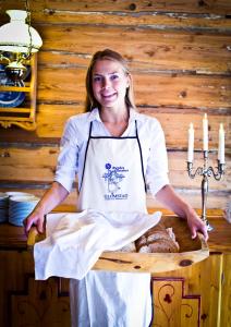 a woman in an apron standing at a table with bread at Glomstad Gjestehus in Tretten