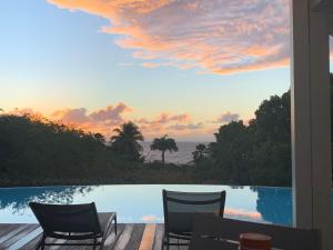 a patio with two chairs and a pool with a sunset at Villa Kouleur Kafé in Sainte-Anne