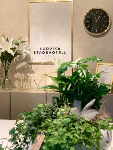 a clock on a wall next to a table with plants at Ludvika Stadshotell in Ludvika