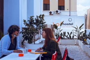 a woman sitting at a table in front of a building at LoL Hostel Siracusa in Syracuse