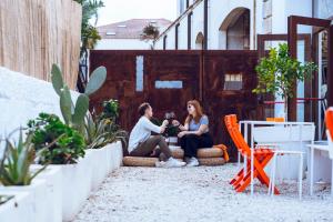 due donne sedute su una panchina in un cortile con piante di LoL Hostel Siracusa a Siracusa