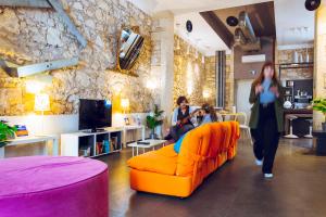 two women walking around a living room with an orange couch at LoL Hostel Siracusa in Siracusa