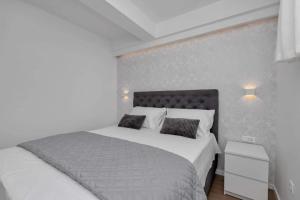 a bedroom with a white bed and a gray wall at Apartman Pelagos in Živogošće