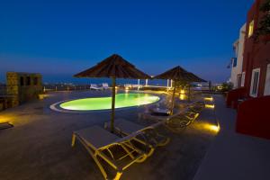 a swimming pool with lounge chairs and umbrellas at night at Thea Luxury Resort in Fira