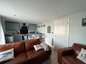 a living room with a brown couch and a kitchen at Orchard Lodge -Coastal Retreat, new build, village views, private garden and terrace in Saint Brides Major