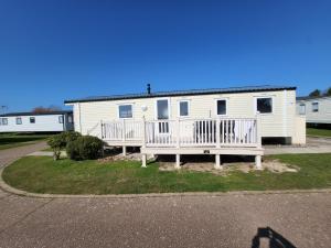 un mobile home blanc avec une terrasse couverte et une maison dans l'établissement Parkdean Kessingland Beach Holiday Chalet, à Benacre