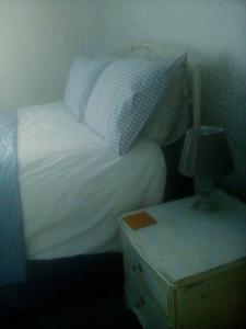 a bed with white sheets and a lamp on a night stand at Welsh Homestay in Cardiff
