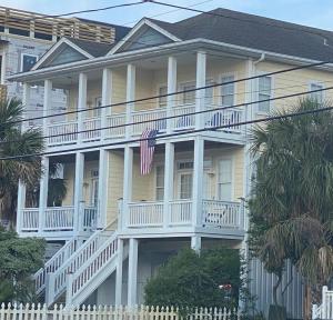 una gran casa amarilla con una bandera americana en el porche en The Manifestation Destination en Carolina Beach