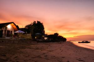 um pôr do sol na praia com uma casa e um barco em Sari Nadi Beach em Nusa Penida