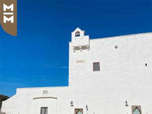 un edificio blanco con una torre de reloj encima en Masseria Mangiato 1557, en Alberobello