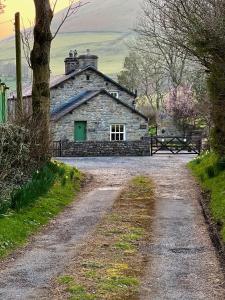 a stone house with a green door on a dirt road at Cross Haw Cottage in Sedbergh