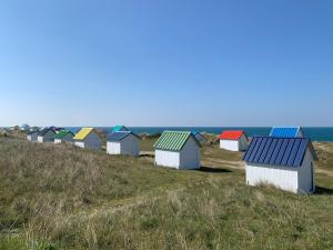 uma fileira de coloridas cabanas de praia numa colina perto do oceano em Gîtes grands groupes - Château des Forges Gouville em Gouville-sur-Mer