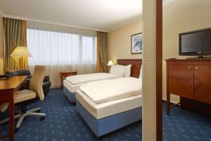 a hotel room with two beds and a desk and a television at H4 Hotel Kassel in Kassel