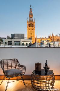 Zimmer mit einem Stuhl, einem Tisch und einem Uhrturm in der Unterkunft Hommyhome Conteros Cathedral Apartments in Sevilla