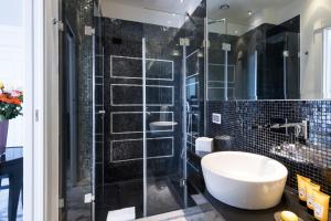 a bathroom with a tub and a shower with black tiles at Hotel Metropole Taormina in Taormina