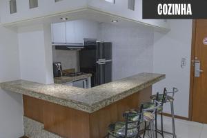 a kitchen with a counter with a refrigerator and stools at Flat Pasárgada 404 in Vila Velha