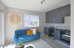 a living room with a blue couch and a kitchen at Modern Studio Apartment in Blouberg in Cape Town