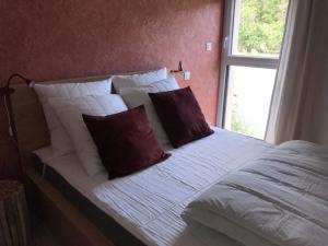 a bed with white sheets and red pillows next to a window at Les 4 gites de la Saisse in Pont-de-Poitte