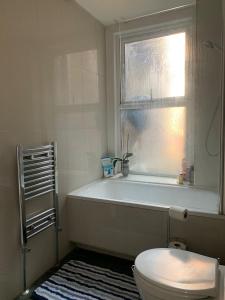 a bathroom with a tub and a toilet and a window at London Spacious Apartment by DC London Rooms in London