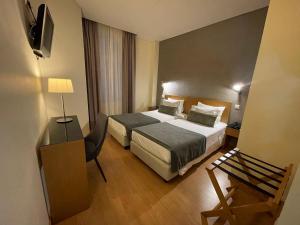 a hotel room with a bed, desk, chair and a lamp at Hotel Sete Colinas in Lisbon