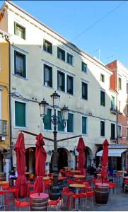 un edificio con mesas, sillas rojas y luz de la calle en Casa BuIIo, en Chioggia