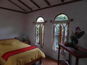 a bedroom with two windows and a bed and a table at Hospedaje Higueron in Baños