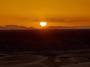 a sunset over the desert with mountains in the background at Riad Mamouche in Merzouga