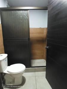 La salle de bains est pourvue de toilettes et d'une douche avec une porte. dans l'établissement Hogar tico-estadounidense cerca de aeropuerto, à Alajuela
