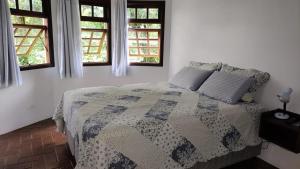 um quarto com uma cama com uma colcha e 2 janelas em Centro - São Francisco Xavier - Casa Agradável em São Francisco Xavier