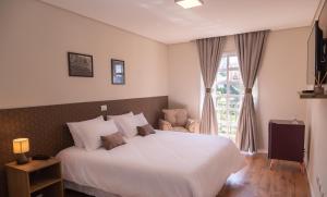 um quarto com uma grande cama branca e uma janela em Village de Charme em Campos do Jordão