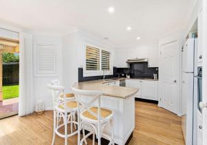 a kitchen with white cabinets and a counter with stools at Beach Haven in Shoalhaven Heads