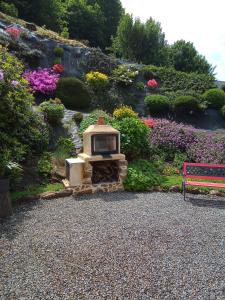 a stone fireplace in a garden with flowers and a bench at Les Hortensias in La Poultière
