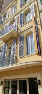 a yellow building with blue shutters and a sign on it at Nouvel Hotel in Saint-Raphaël